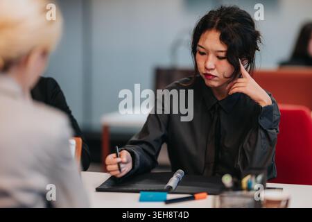 Young business woman taking notes during a focused meeting in a modern office setting Stock Photo