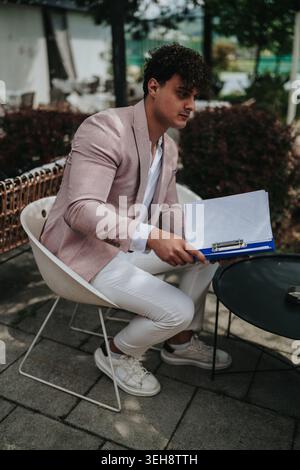 Man in pink blazer sitting at an outdoor cafe holding a clipboard and reviewing documents Stock Photo