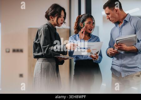 Three colleagues discussing charts and notes during a collaborative business meeting in an office Stock Photo