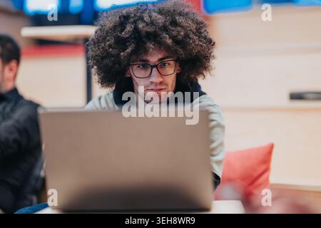 Young man working on laptop in a modern coworking space, focused on studying and coding Stock Photo