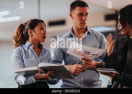 Three colleagues discussing documents in a business meeting while reviewing charts and notes Stock Photo