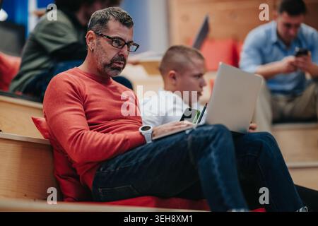 Middle-aged man working on laptop in casual coworking space among colleagues Stock Photo
