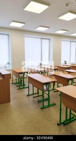 classroom interior showing aligned desks and chairs under bright daylight from windows. classroom without students, learning environment, school conce Stock Photo