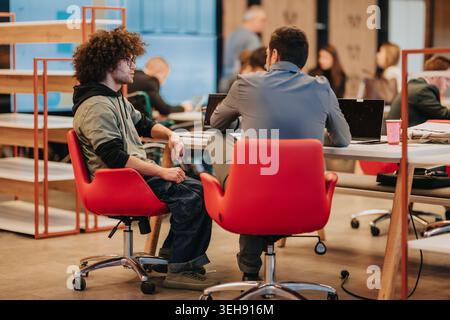 Business meeting between two young professionals in a casual coworking space with laptops and conversation Stock Photo