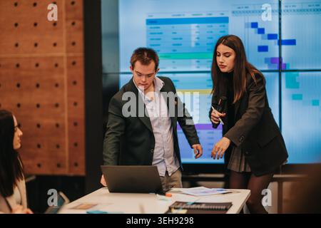 Business colleagues presenting project data on laptop and large screen during collaborative meeting Stock Photo
