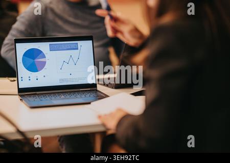 Business meeting with laptop showing charts and colleagues discussing data at a desk Stock Photo