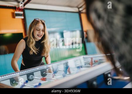 Two friends playing foosball at an indoor arcade table enjoying a casual game together Stock Photo