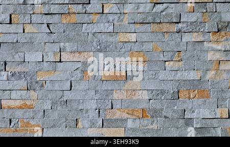 Wall made of reconstructed stone bricks of gray and red colors. Modern rustic coating for exterior or interior. Background and texture. Full frame. Stock Photo
