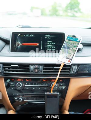 Phone screen with route directions connected via charging cable on the vehicle central console panel. Concept of smart city driving assistance system. Stock Photo
