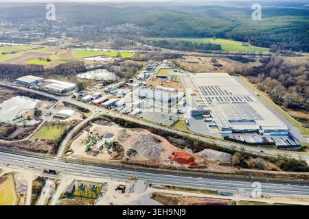 Aerial view of large industrial warehouses and a gravel quarry surrounded by lush green forests and rolling hills in Buttenheim, Bavaria, Germany. Stock Photo