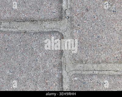 A concrete road surface shows visible cracks and texture. This surface is common in urban settings. Light shines on the road making its features appar Stock Photo