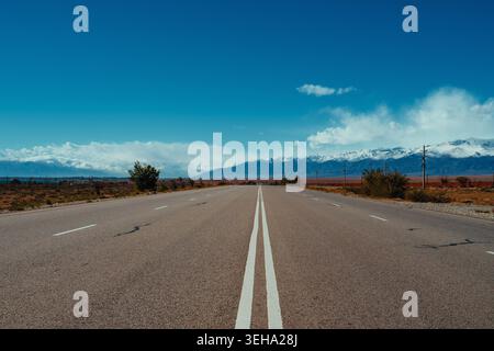 Lonely road with double solid line on sunny day with mountains Stock Photo