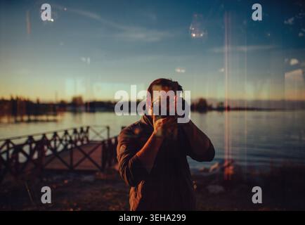 Man taking selfie in window reflection with lake and pier in background Stock Photo