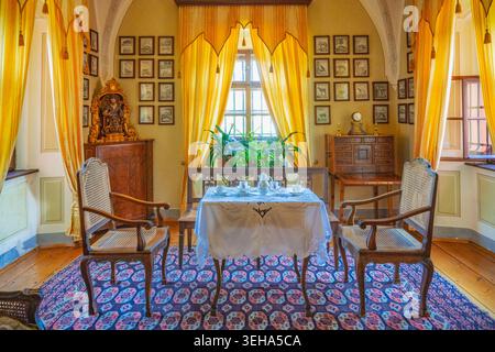 In Cervena Lhota Castle, the dining area shows elegant chairs and a table set with tableware. Large curtains frame the window, allowing light to brigh Stock Photo