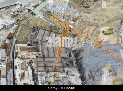 Aerial view of a construction site with a large yellow tower crane, workers on a rebar foundation, and heavy machinery in Sariyer, Istanbul, Turkiye. Stock Photo