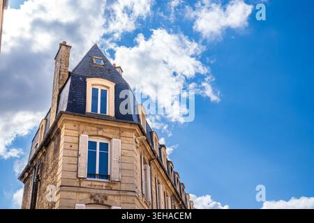 Elegant facade of a historic building made of Caen stone under a deep blue sky with white clouds. The photo highlights the slate mansard roof, classic Stock Photo