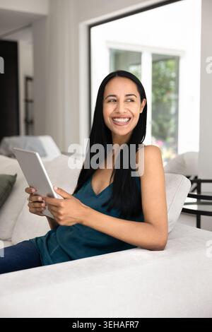 Joyful New-Zealander woman relaxing on sofa with tablet device Stock Photo