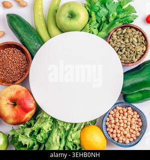 Healthy green fruits, vegetables, nuts and seeds arranged around empty white place on white background. Balanced diet concept and copy space for healt Stock Photo