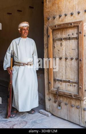 An armed guard in traditional Omani attire with turban (massar) a long ...
