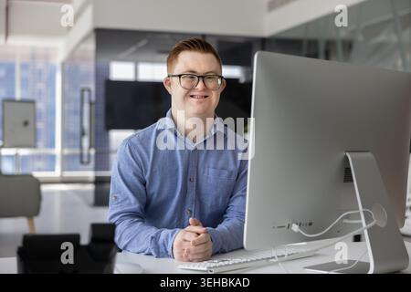 Man with Down syndrome sit at desk with computer, portrait Stock Photo