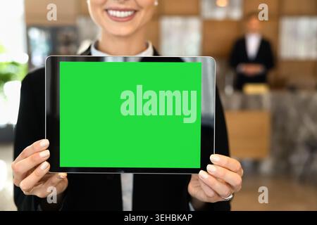 Female receptionist presenting digital tablet displaying green mockup blank screen Stock Photo