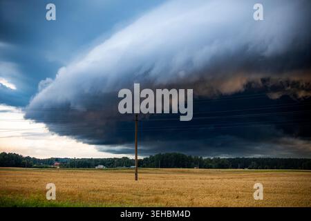 Dramatic supercell storm cloud moving over rural farmland with dark shelf clouds and threatening summer weather in Lithuania. Stock Photo