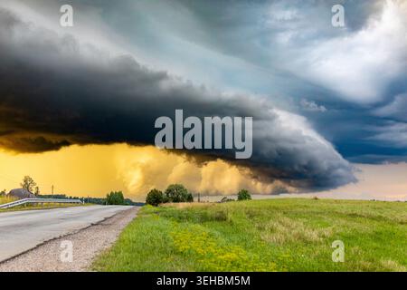 Dramatic supercell shelf cloud over rural road and green fields during severe summer thunderstorm in the Lithuanian countryside. Stock Photo