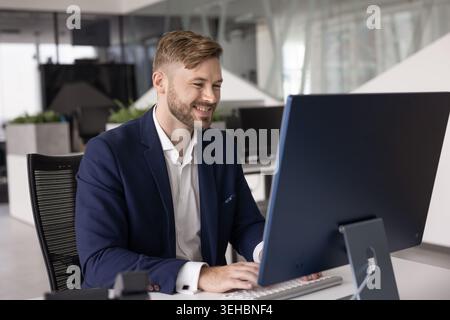 Confident young Caucasian businessman in suit working at desktop computer Stock Photo
