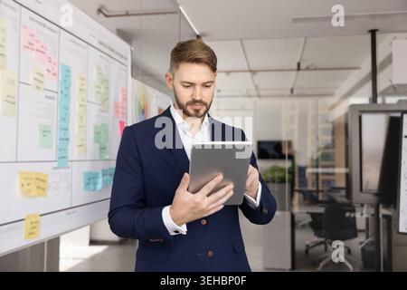 Professional focused man stands in office using digital tablet Stock Photo