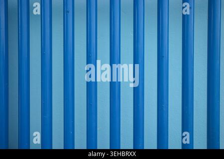 Vertical blue metal bars fence creating a modern geometric pattern background texture in an urban industrial environment. Stock Photo
