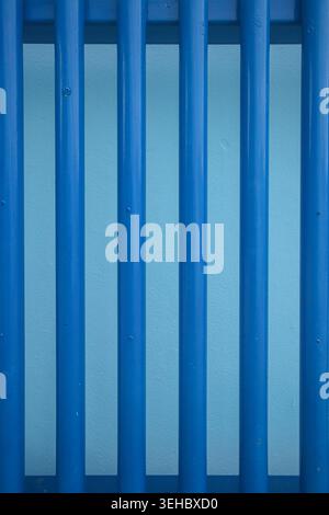 Vertical blue metal bars fence creating a modern geometric pattern background texture in an urban industrial environment. Stock Photo