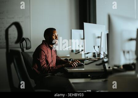 A dedicated professional works intently at his computer in a sleek office space illuminated by soft light during evening hours. Stock Photo