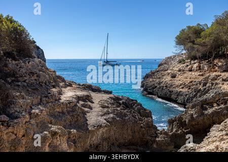 Peaceful coastal view with a sailboat floating on clear blue water surrounded by steep rocky cliffs near Sa Calobra on Mallorca west coast Stock Photo