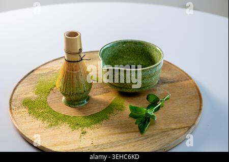 Matcha tea ceremony setup with fresh herbs and mint leaves in garden-like atmosphere. Bowl with whisk and organic accessories on wooden tray with verd Stock Photo