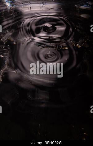 454.Close-up of water surface showing concentric ripple rings from central impact. High-contrast lighting highlights wave symmetry and texture. Image Stock Photo