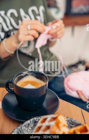 woman knitting with pink yarn and needles while drinking coffee in cozy cafe or home interior close up of hands creating handmade textile hobby Stock Photo