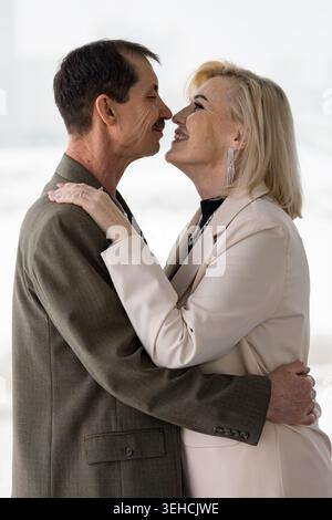 Tender Caucasian Couple Kissing In Office, Mature Professionals Sharing Quiet Reunion Near Window, Blazer And Suit Attire, Soft Gaze And Forehead Stock Photo