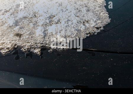 Melting snow and ice texture on black car surface during winter thaw Stock Photo