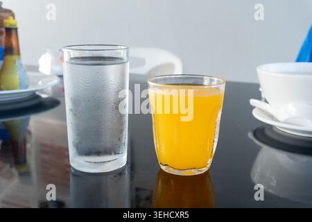 A set of drinking water and orange juice in transparent glassess is served to guests on the table in a restaurant. Stock Photo
