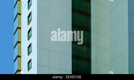 A vertical geometric detail of a contemporary building exterior featuring glass windows and white architectural panels under clear daylight Stock Photo