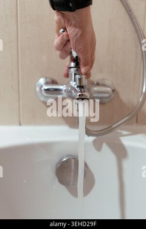 Hand turning on chrome bathtub faucet with water flowing into the tub Stock Photo