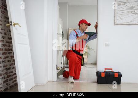 Male worker with electric drill installing door strike plate at home Stock Photo