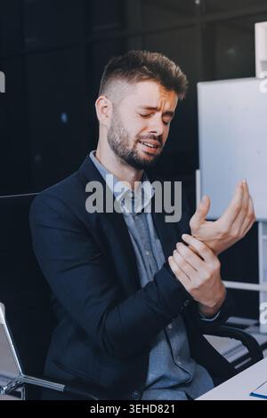 A man with a sore throat works inside the office, a businessman at work has a sore throat flu and cold, uses a laptop at work. Stock Photo