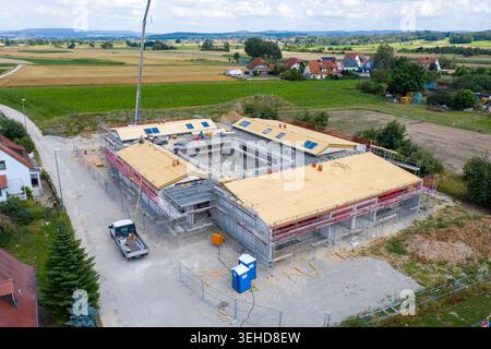 Igensdorf, Germany - 11 May 2024: Aerial view of a large building under construction with scaffolding, a crane arm, and workers on the roof, surrounde Stock Photo