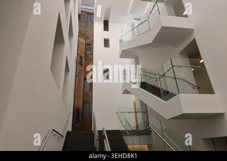 The modern atrium and staircase extension contrasting with the historic brick wall inside John Rylands Library in Manchester, England, UK Stock Photo