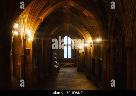 A vaulted neo-Gothic stone corridor lit by electric lamps inside the John Rylands Library in Manchester, England, UK Stock Photo