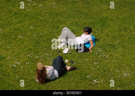 An overhead view of two people relaxing on a green grass lawn with daisies in a park in Manchester, England, UK. Stock Photo