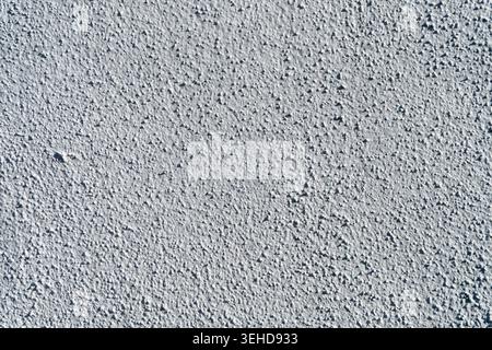Textured gray wall stucco surface with small bumps is bathed in bright, even light, creating a granular pattern. Stock Photo
