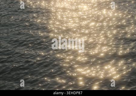 Abstract summer water background with shimmering golden reflections and glittering sunlight across gentle waves. Stock Photo