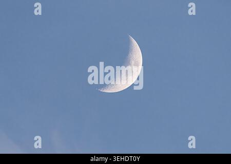 Gentle night sky. Peaceful crescent moon resting beneath pale blue canopy of clouds. Serene crescent moon softly illuminated against light blue sky wi Stock Photo